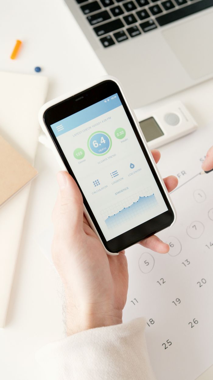 A person holding a smartphone displaying a health monitoring app near scheduling items.